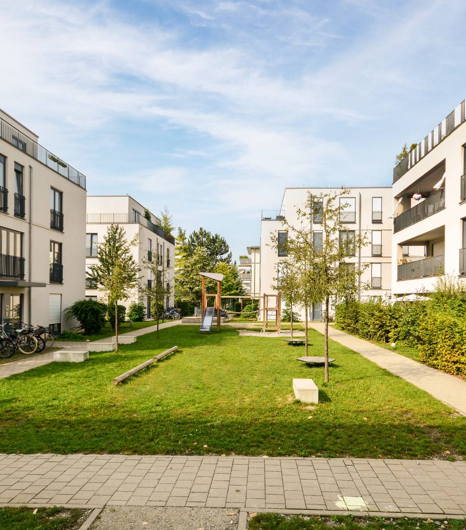 Modern residential buildings surrounding a green communal lawn under a blue sky.