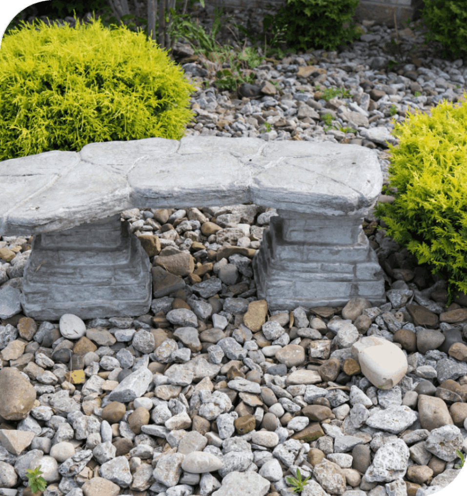 Stone bench on gravel with green bushes.